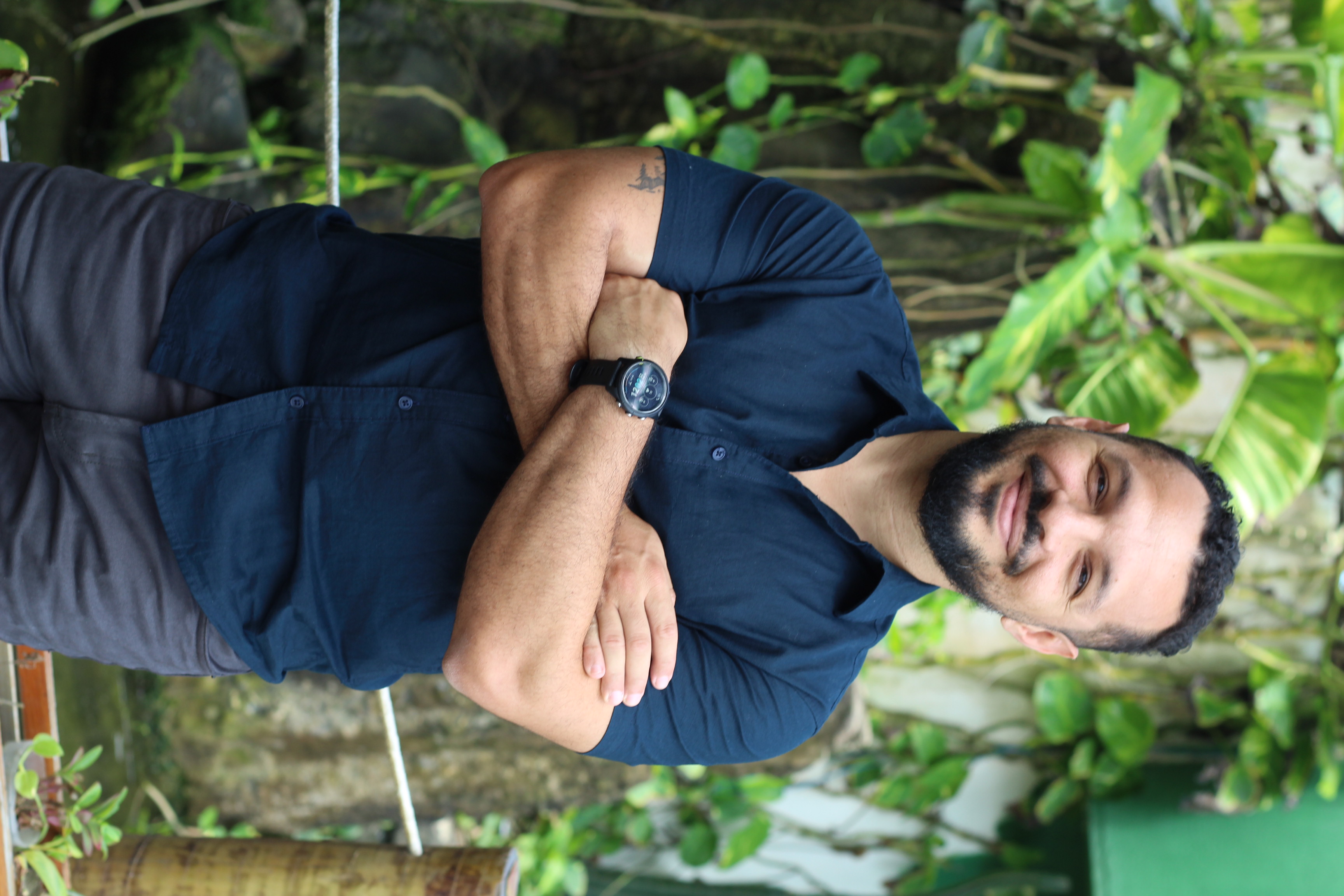 Adriano Diamarante em pé, de braços cruzados, sorrindo, em meio a plantas.